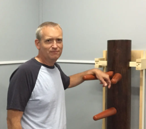 Man standing beside a wooden training dummy.
